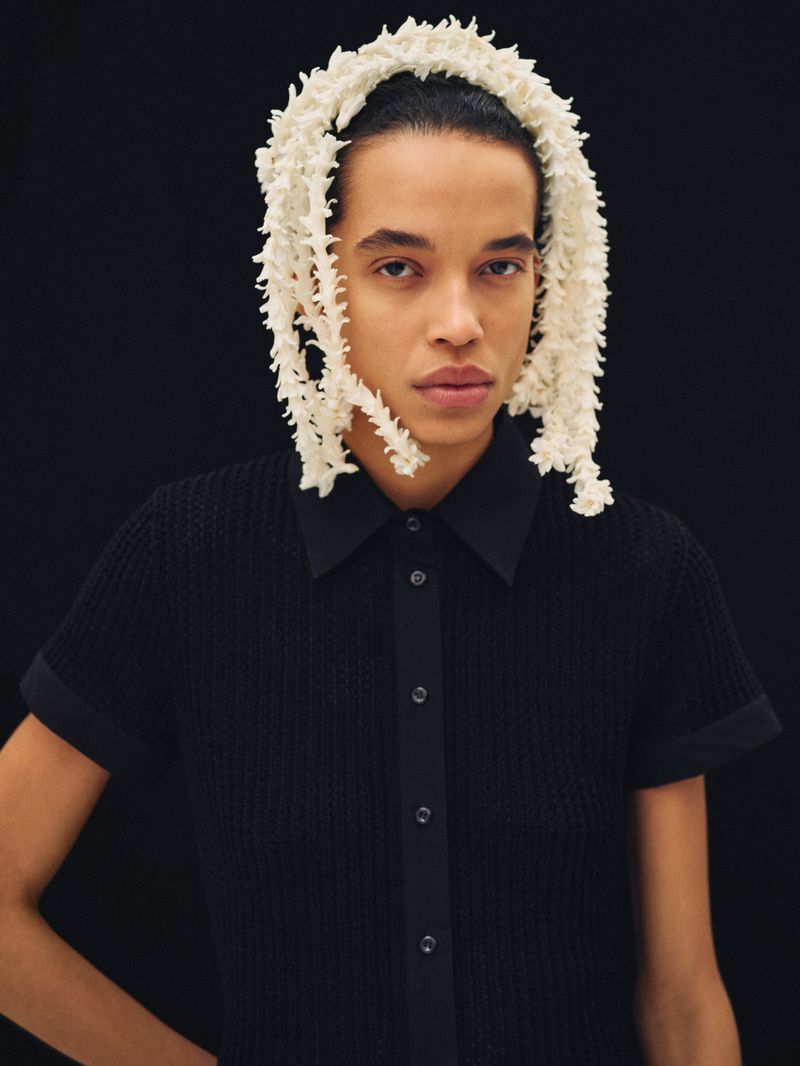Model wearing a black buttoned collared top and white floral headpiece against a dark background for Exit Magazine.