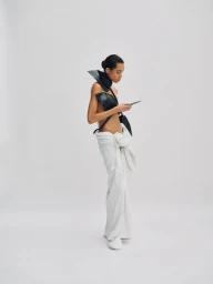 Model Lara Menezes wearing sculptural black top and white trousers against a white seamless studio backdrop.