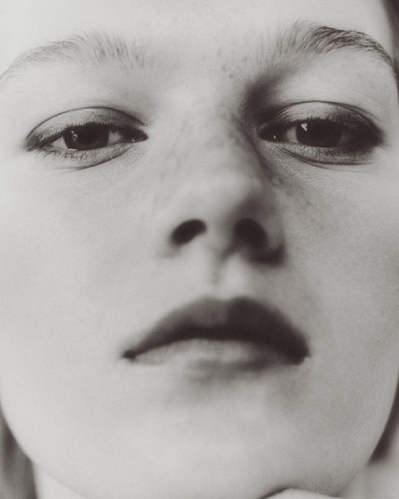 Close-up portrait of a model featuring soft lighting, detailed eye makeup, and subtle freckles.
