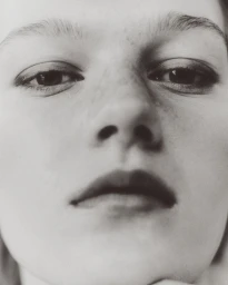 Close-up portrait of a model featuring soft lighting, detailed eye makeup, and subtle freckles.