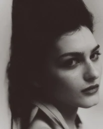 Close-up monochrome portrait of a model with voluminous dark hair and dark lipstick against a plain studio background.