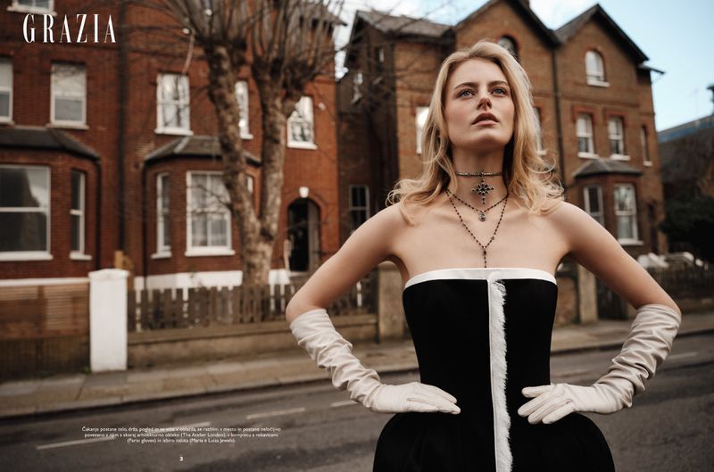 Woman in black and white strapless gown with long opera gloves standing before brick residential buildings.