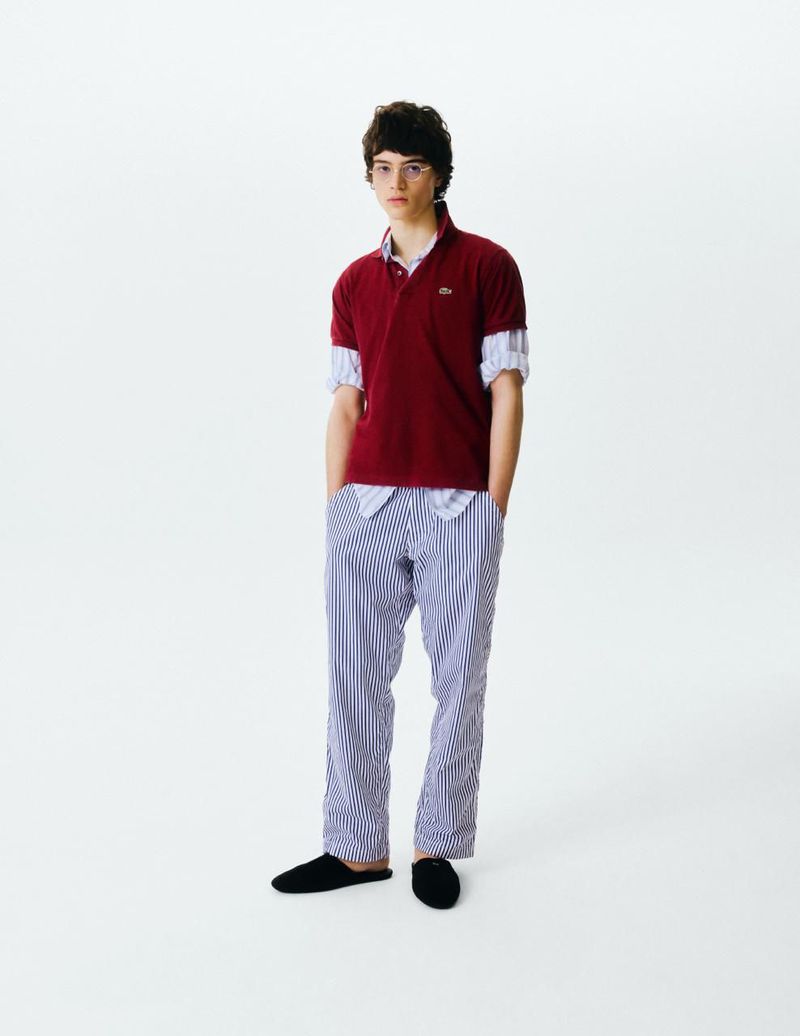 Model wearing a red polo shirt layered over a striped shirt and matching trousers against a plain white background