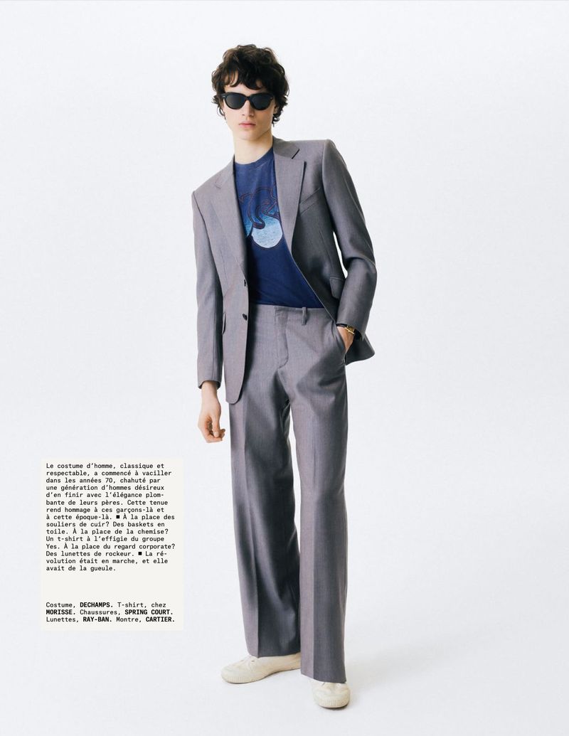 Model wearing grey suit jacket and trousers with blue graphic t-shirt against white background