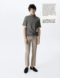 A young male model standing against a white seamless background wearing a striped turtleneck t-shirt and grey trousers.