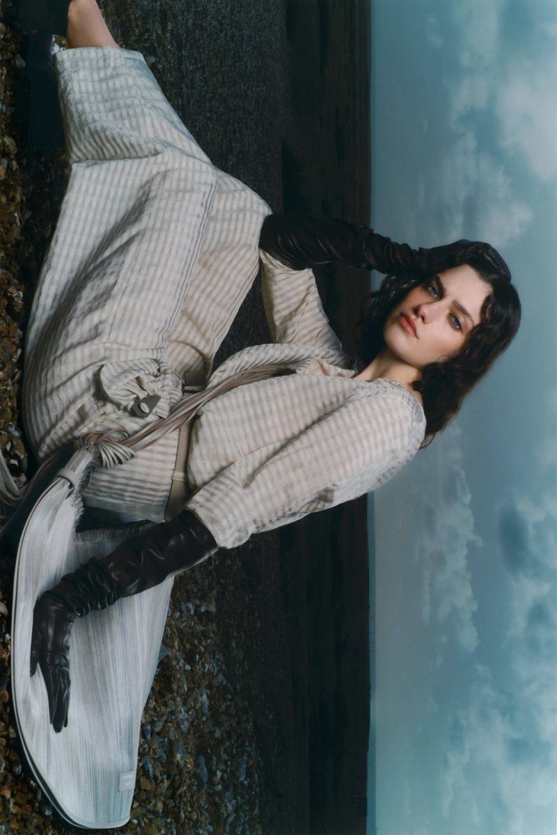 Model wearing patterned outfit and dark leather gloves posing outdoors against a cloudy sky backdrop