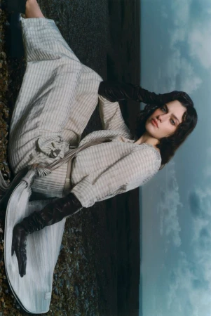 Model wearing patterned outfit and dark leather gloves posing outdoors against a cloudy sky backdrop