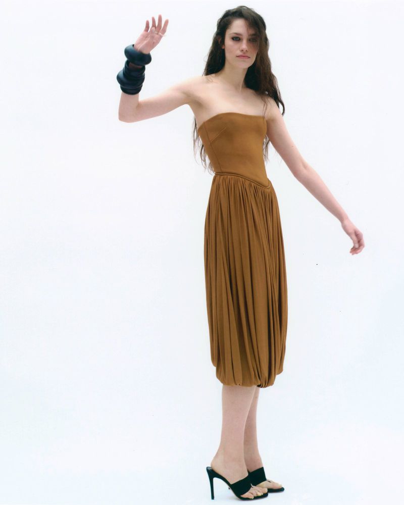 Model in a brown strapless dress wearing chunky black bracelets against a white background