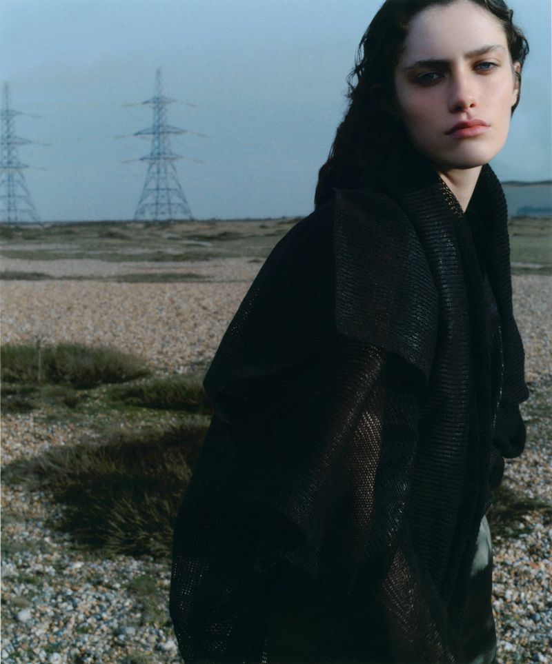 Model in black textured top outdoors on a pebble landscape with power pylons under an overcast sky for Silhouette Magazine