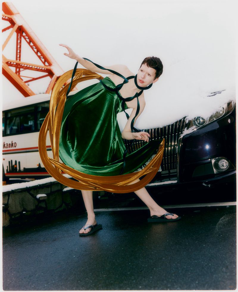 Model in green dress holding a gold ring hoop posing near a car and red bridge structure for Grazia Malaysia Tokyo Park editorial