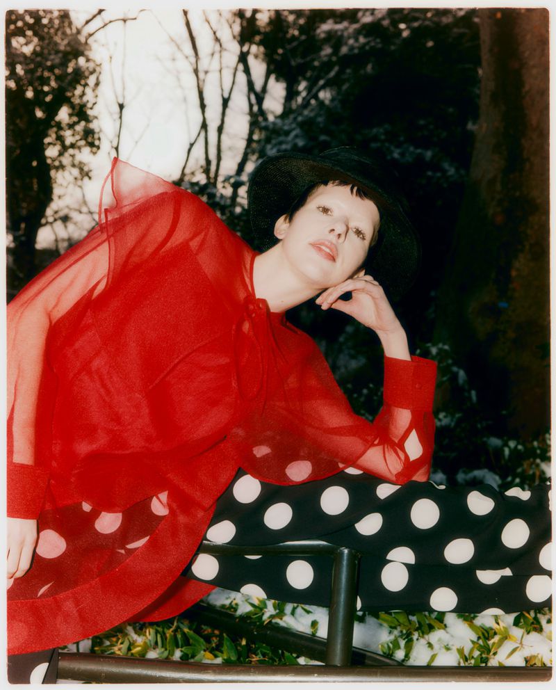 Model in sheer red blouse and black polka-dot trousers wearing a black hat outdoors in Tokyo Park for Grazia Malaysia