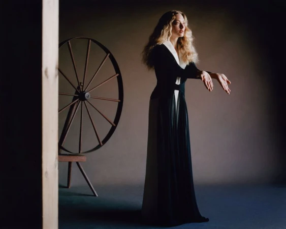 Amanda Seyfried wearing a long black and white dress near a spinning wheel in a studio portrait for American Vogue.