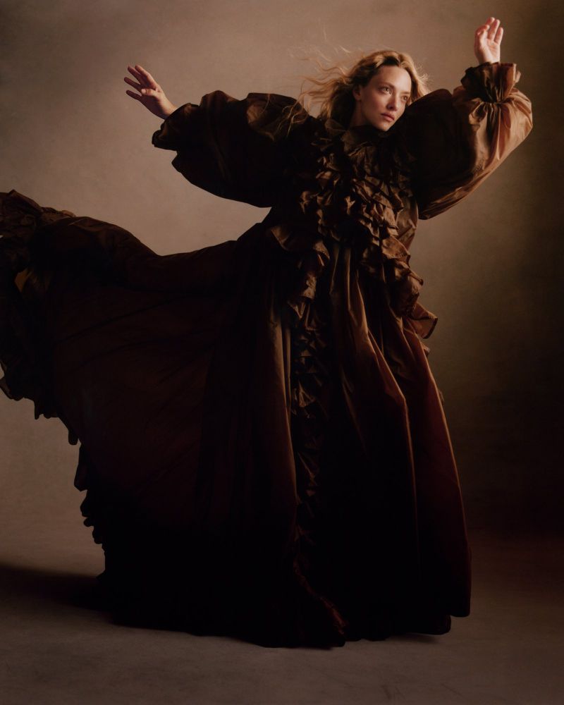 Amanda Seyfried wearing a voluminous brown ruffled gown against a neutral studio background.