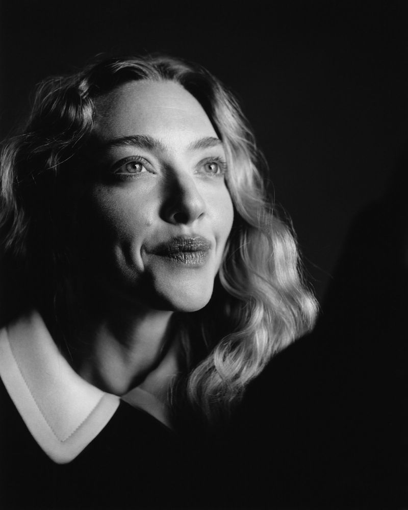 Close-up black and white portrait of actor Amanda Seyfried looking upward with a soft expression against a dark background.