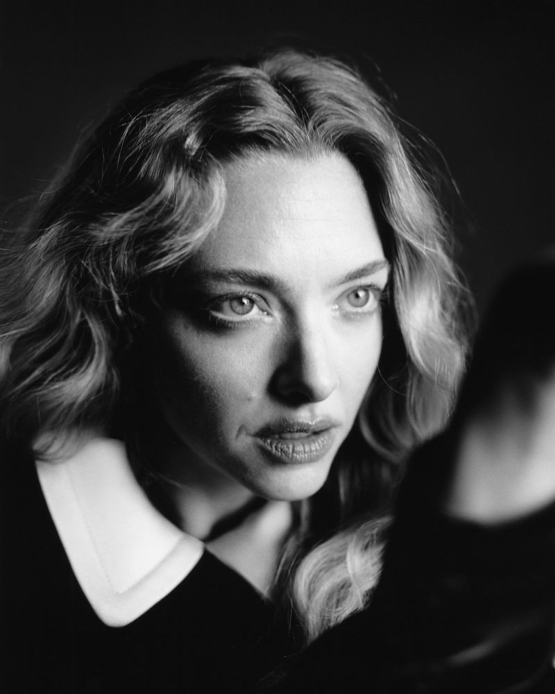 Close-up monochrome portrait of actress Amanda Seyfried with wavy hair against a dark background