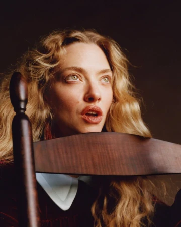 Portrait of Amanda Seyfried leaning against a dark wooden chair for an American Vogue editorial.