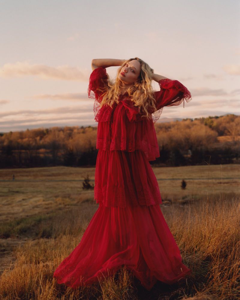 Amanda Seyfried in a red tiered dress posing in a grassy field at sunset for an American Vogue editorial.