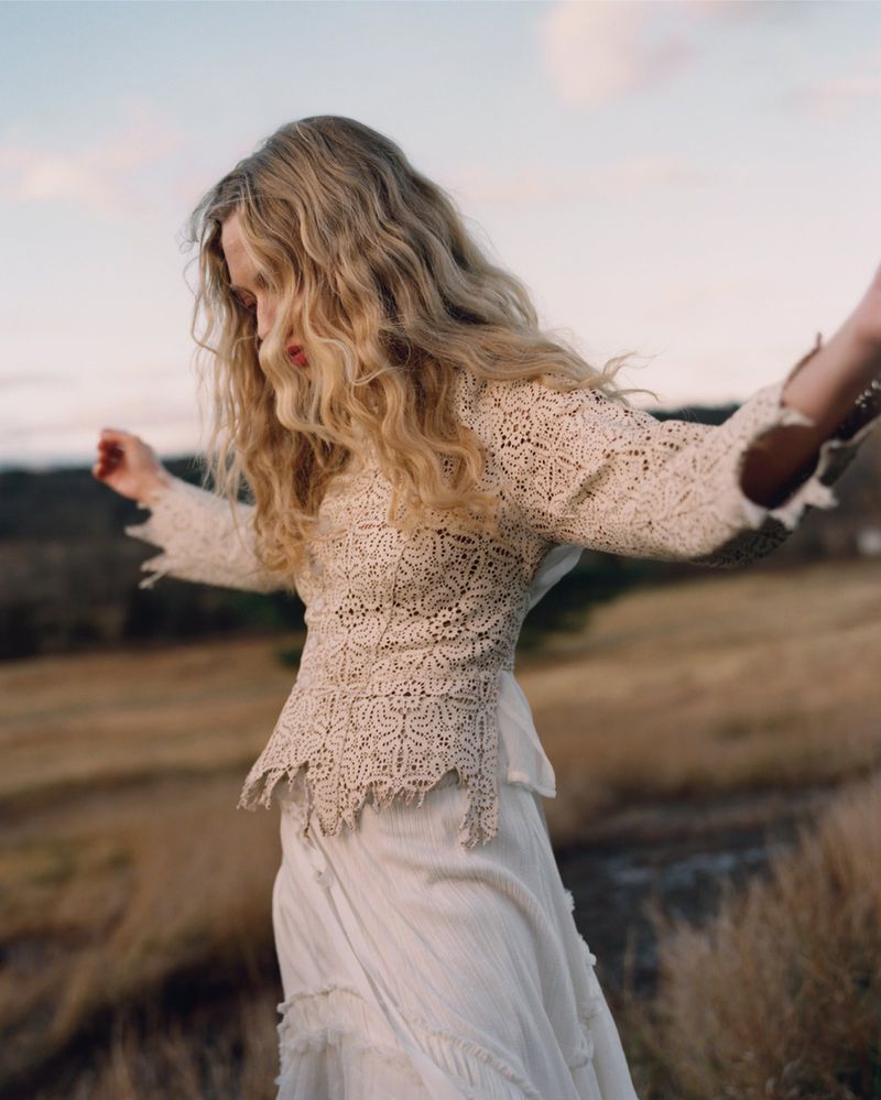 Amanda Seyfried wearing a cream lace top and skirt outdoors in a grassy field at sunset.