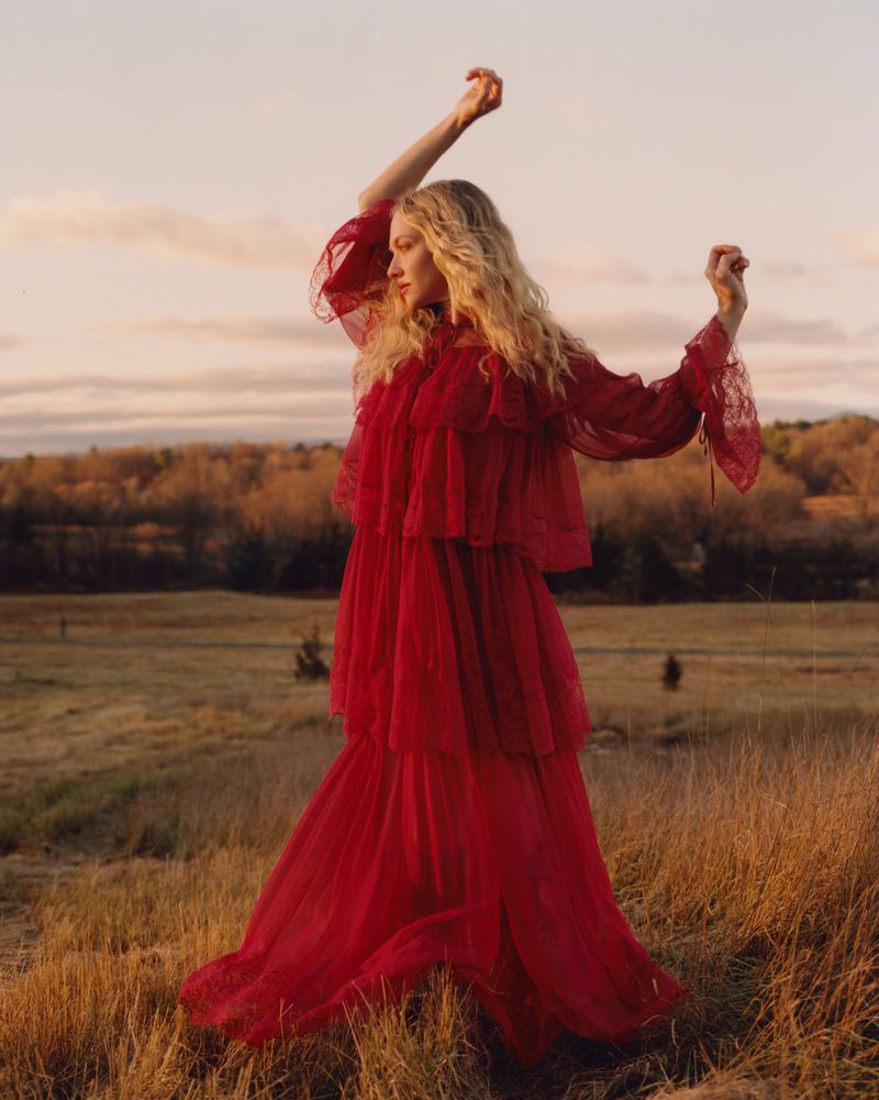 Amanda Seyfried wearing a long red tiered dress in a grassy field at sunset