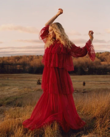 Amanda Seyfried wearing a long red tiered dress in a grassy field at sunset