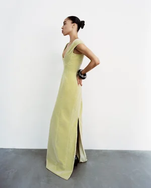 Model Zsela wearing a sleeveless pale yellow floor-length dress and chunky black bracelet against a white studio background.