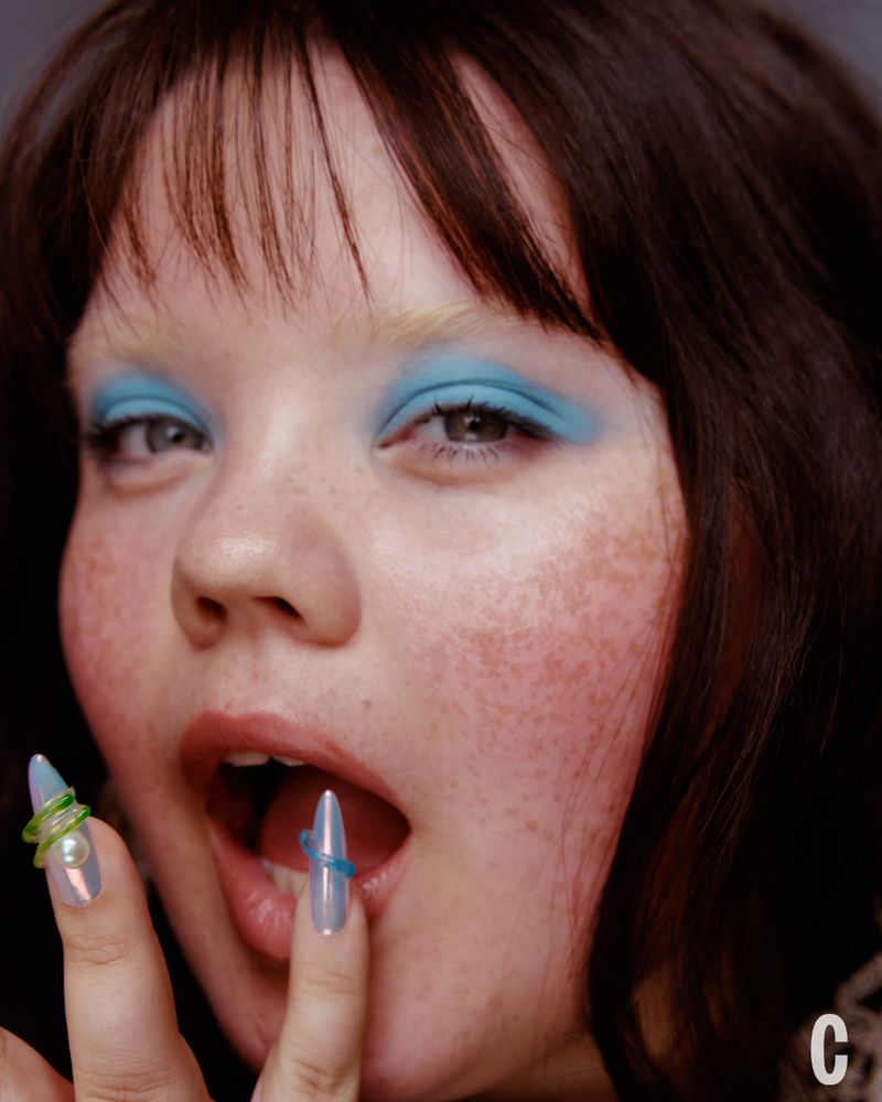 Close-up portrait of a woman with vibrant blue eyeshadow, long pointed manicured nails, and dark bangs for Cosmopolitan US.