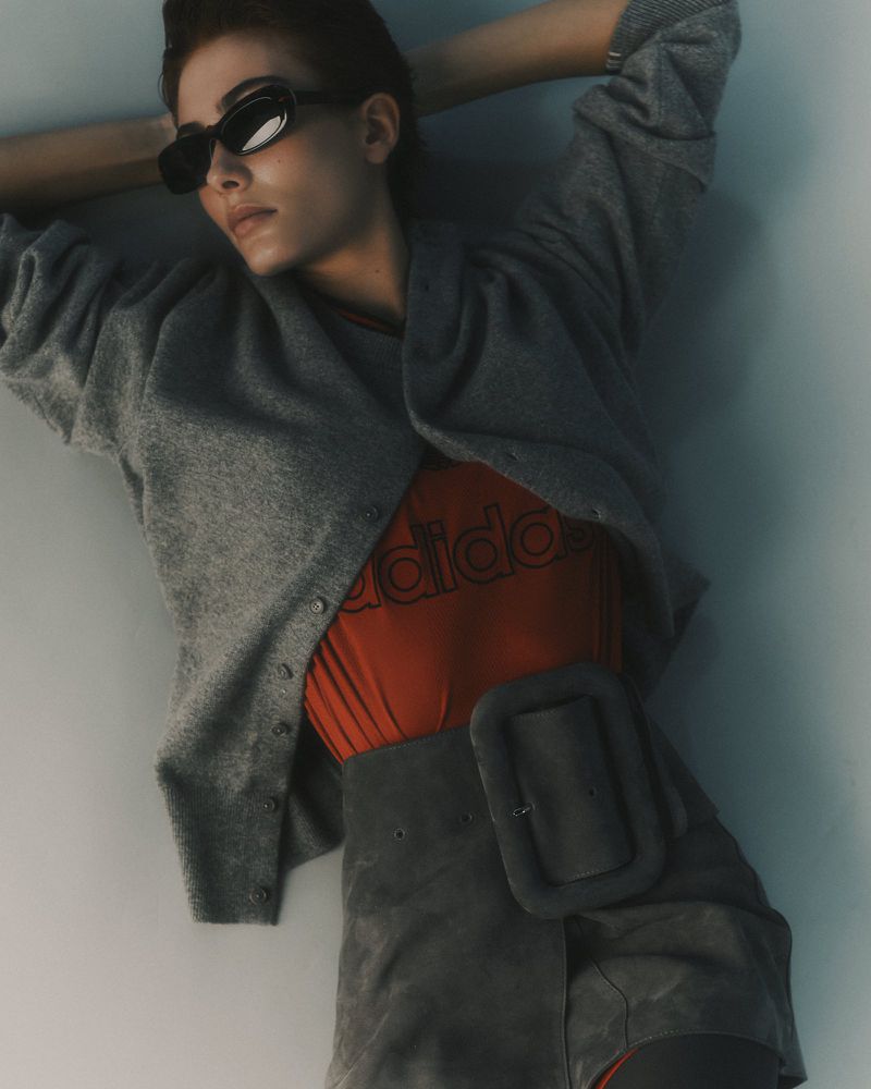 Model in grey cardigan and dark sunglasses posing against a plain background for The Greatest Magazine editorial