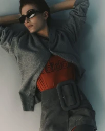 Model in grey cardigan and dark sunglasses posing against a plain background for The Greatest Magazine editorial