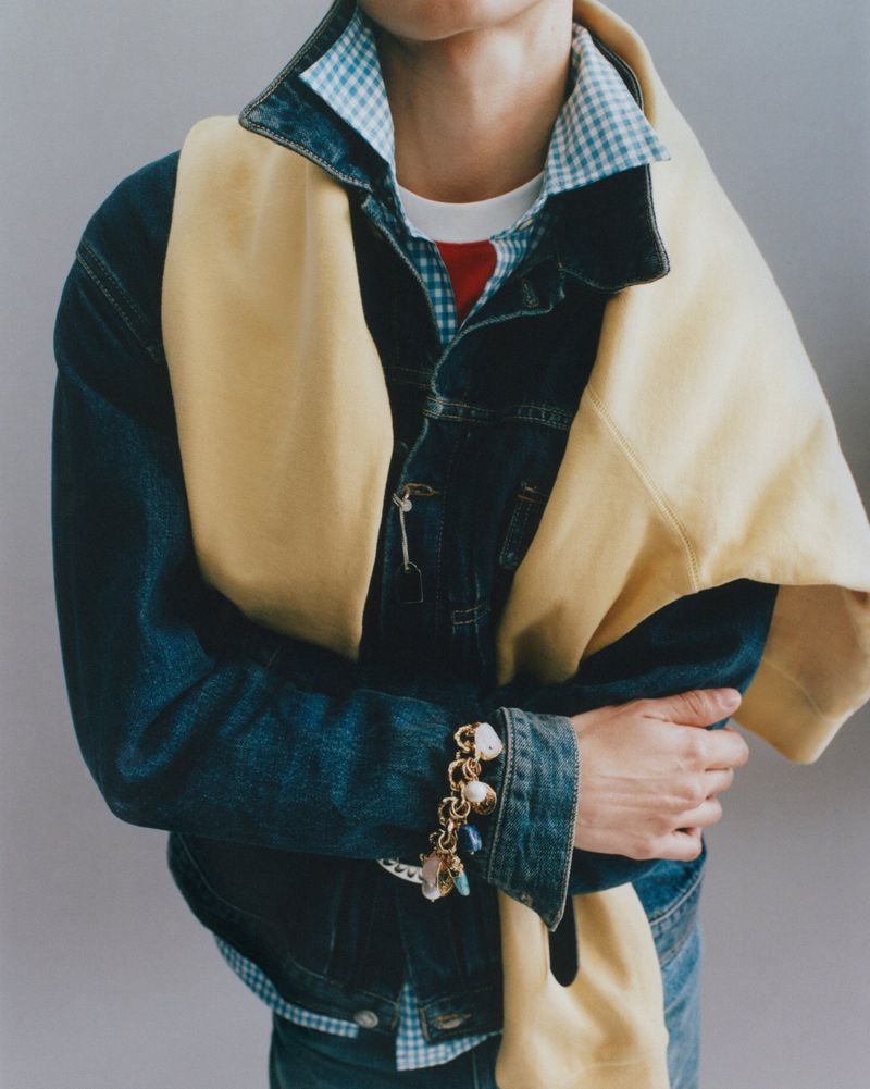 Model wearing layered denim jacket and sweater with charm bracelet for D Repubblica editorial by Xavier Casanueva.