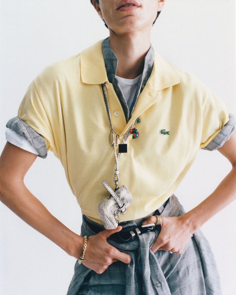 Model wearing layered yellow polo shirt, grey shirt, and trousers against a white background for D Repubblica fashion editorial.