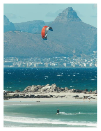 Kitesurfer riding waves on a sunny beach with a large mountain range in the background