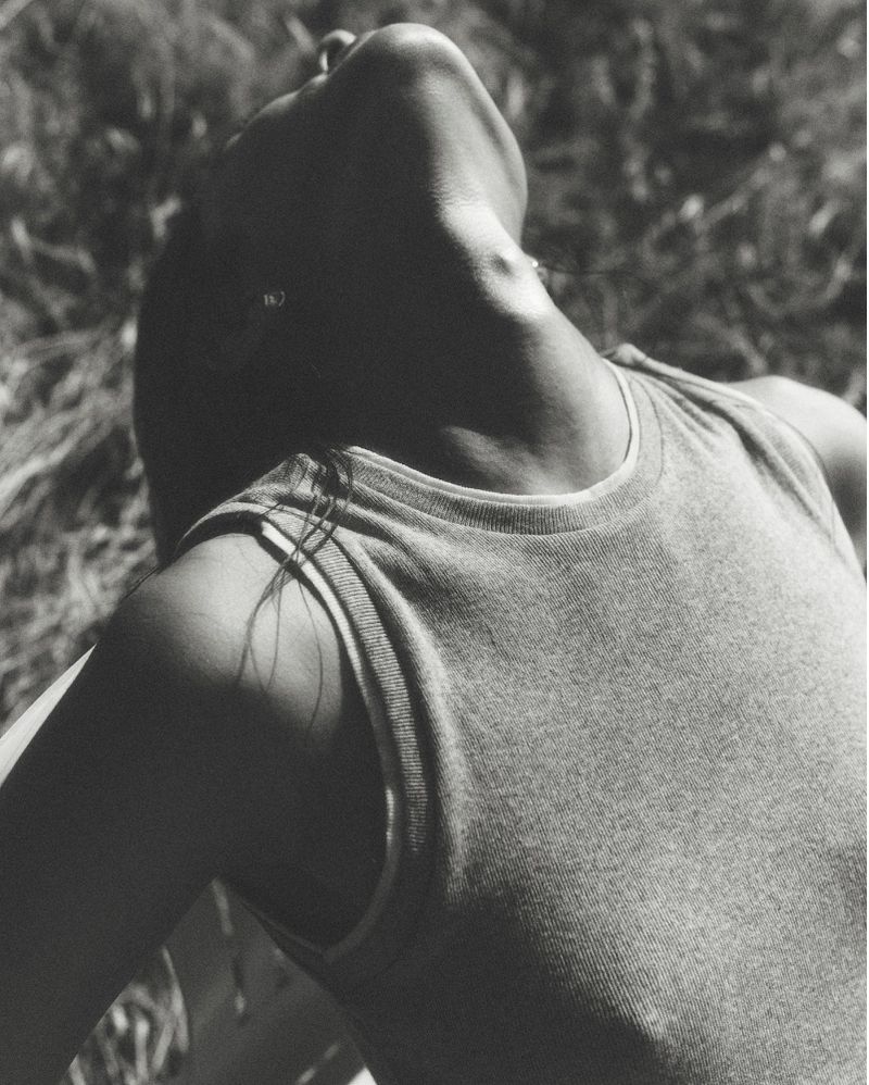 Close-up black and white portrait of a model tilting her head back outdoors against grassy ground