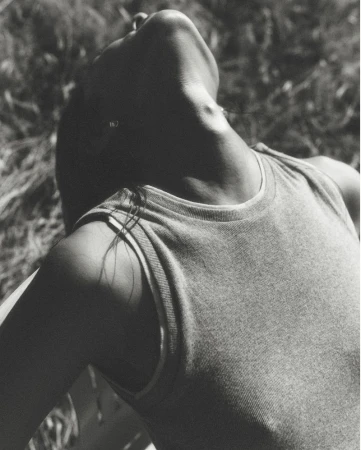 Close-up black and white portrait of a model tilting her head back outdoors against grassy ground