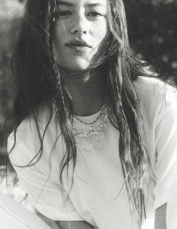 Portrait of Mahalia Celeste Henderson in a white t-shirt wearing layered beaded necklaces outdoors in black and white