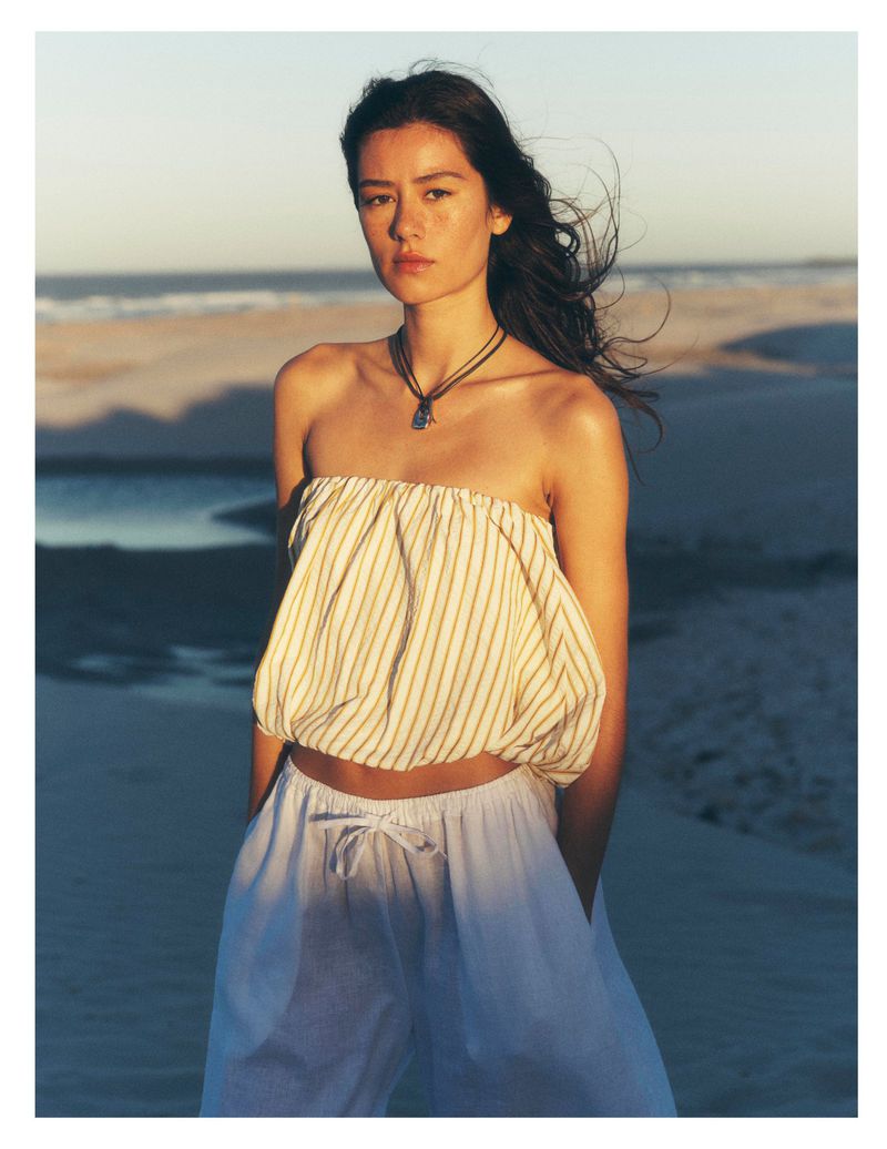 Woman wearing striped strapless top and white trousers on a sandy beach at sunset for Anthropologie Cape Town project