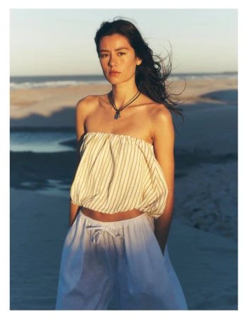 Woman wearing striped strapless top and white trousers on a sandy beach at sunset for Anthropologie Cape Town project