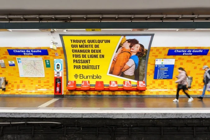 Bumble ad in a subway station featuring a couple embracing, accompanied by French text and the Bumble logo, with people in the background.