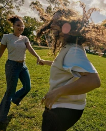 Two women holding hands and laughing while spinning together in a sunny green park