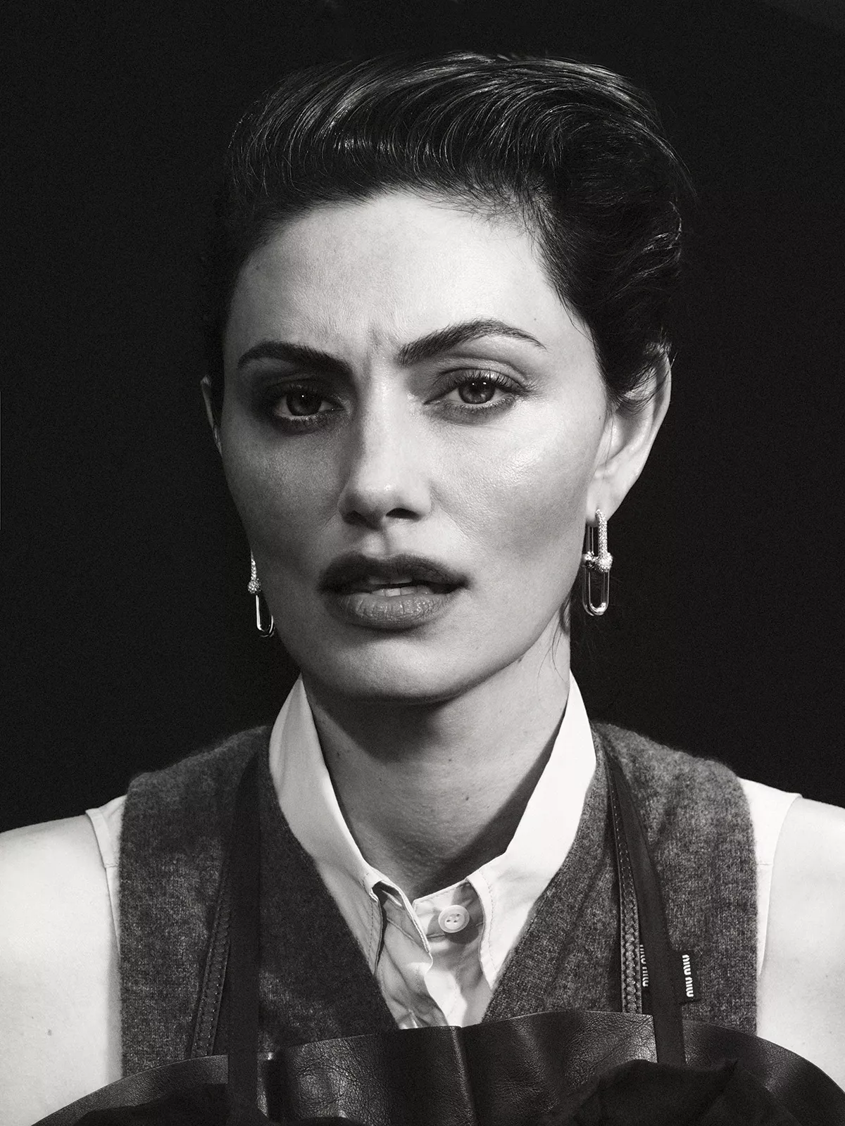Portrait of Phoebe Tonkin wearing a white shirt and dark vest against a dark background for Harper's Bazaar Australia