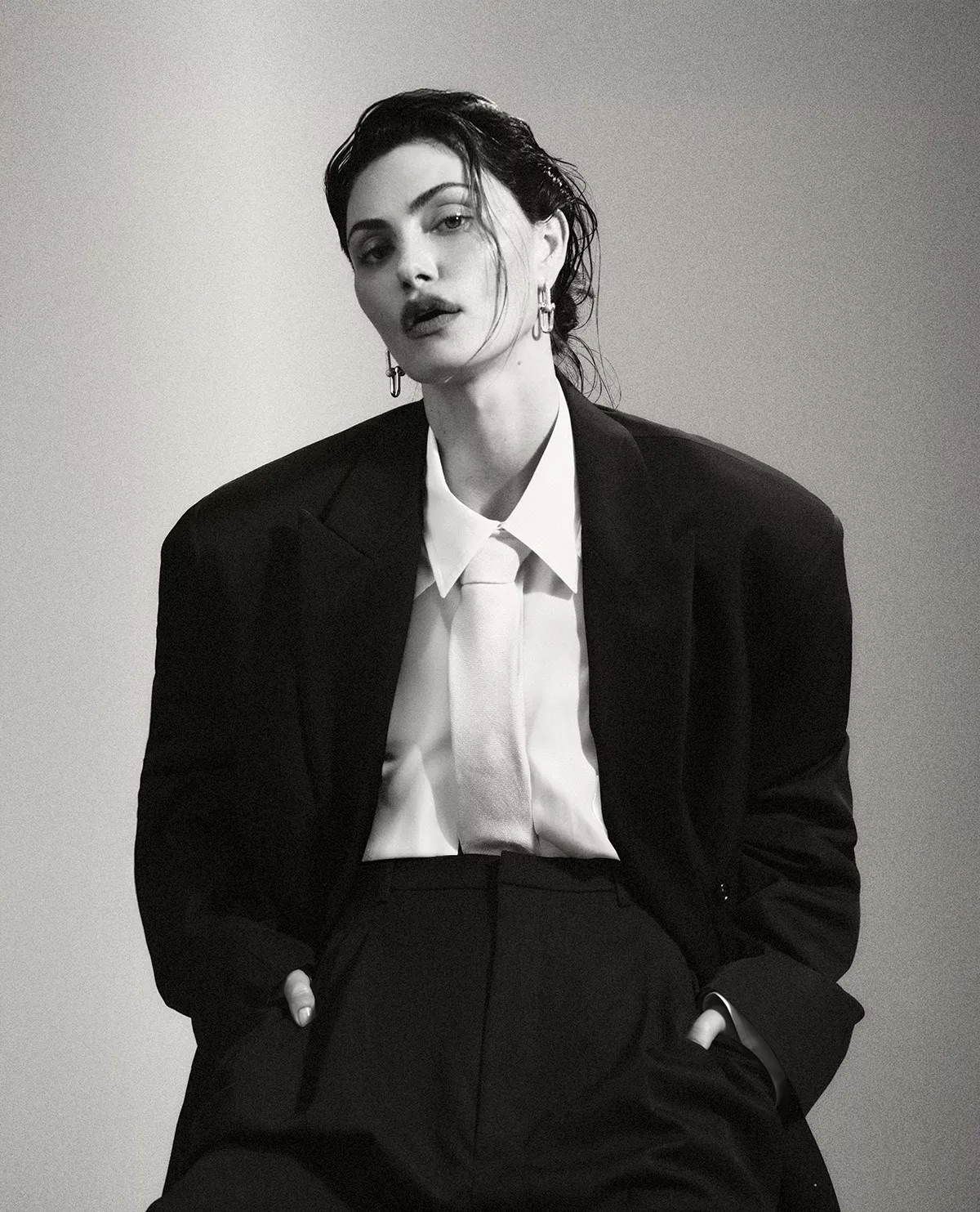 Phoebe Tonkin in an oversized black blazer and white shirt with slicked wet hair against a neutral gradient background