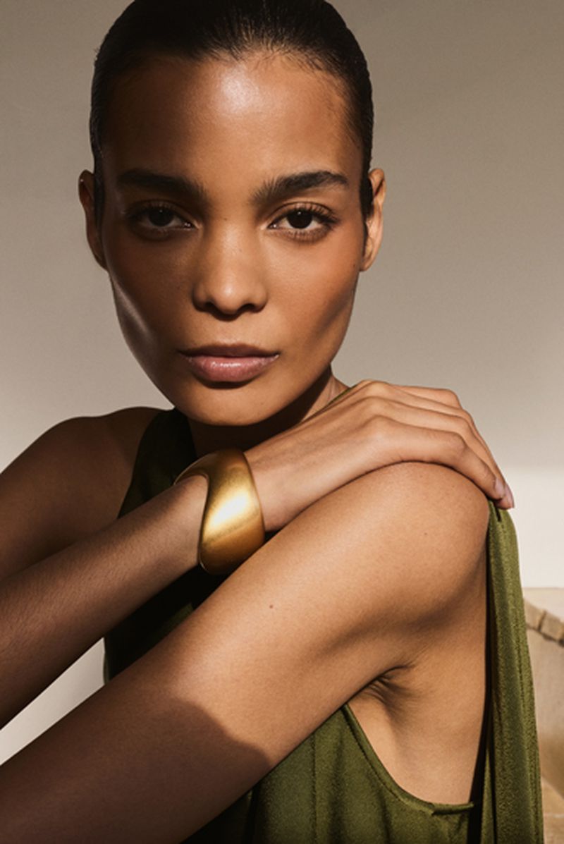 Close-up portrait of a woman wearing an olive green dress and a thick gold cuff bracelet, photographed by Turkina Faso for Reiss.