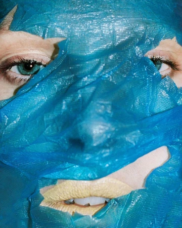 Close-up portrait of a person's face partially covered with a blue plastic material, highlighting their eyes and mouth area.