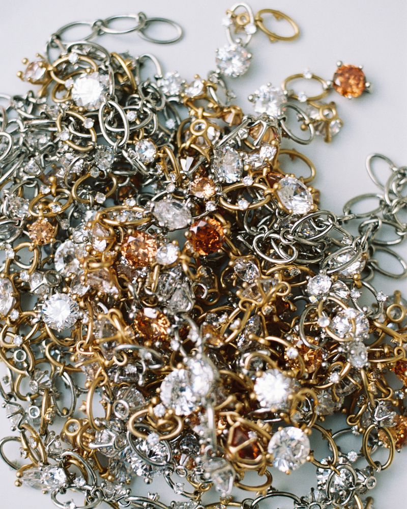 Close-up of a tangled pile of gold and silver chain jewelry, some adorned with clear and peach-colored stones, filling the frame.