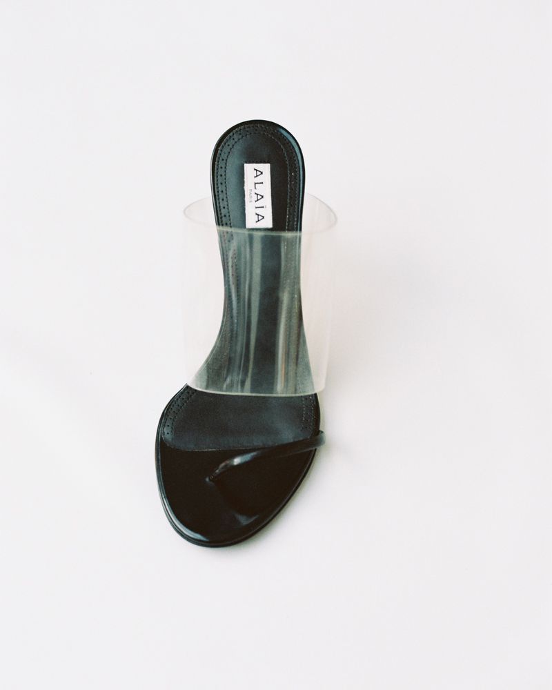 Black Alaïa sandal with a transparent strap on a white background in a studio product shot, highlighting its minimalist design and textures.