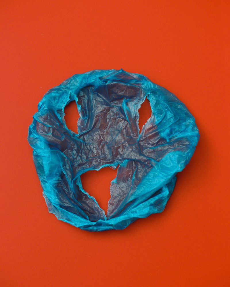Studio shot of a blue plastic bag with several holes against a solid red background, with bright, even lighting and overhead camera angle.