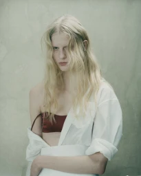 Model with long blonde hair wearing an unbuttoned white shirt and red bandeau top against a pale textured background