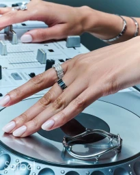 Close-up of manicured hands wearing silver diamond rings and resting near a silver bracelet on a DJ mixer console.