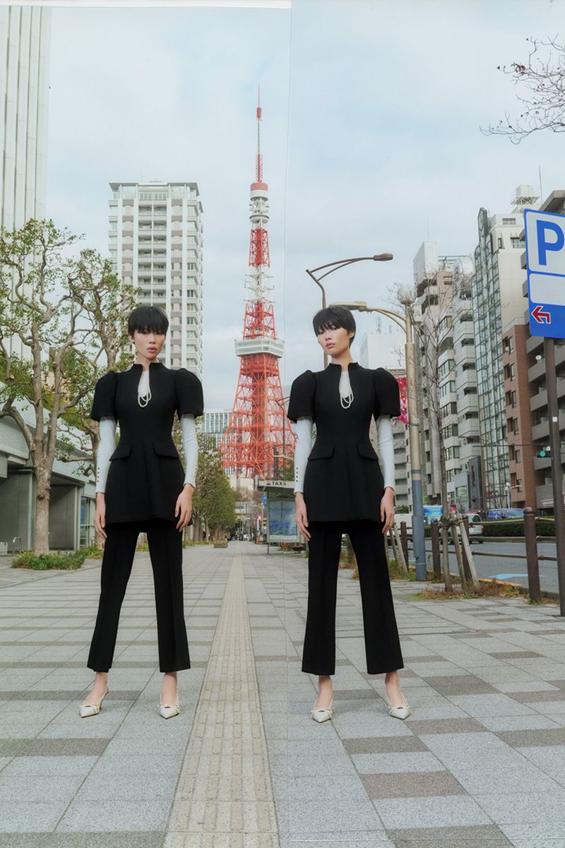 Two models standing on a city street in Tokyo with the Tokyo Tower visible in the background
