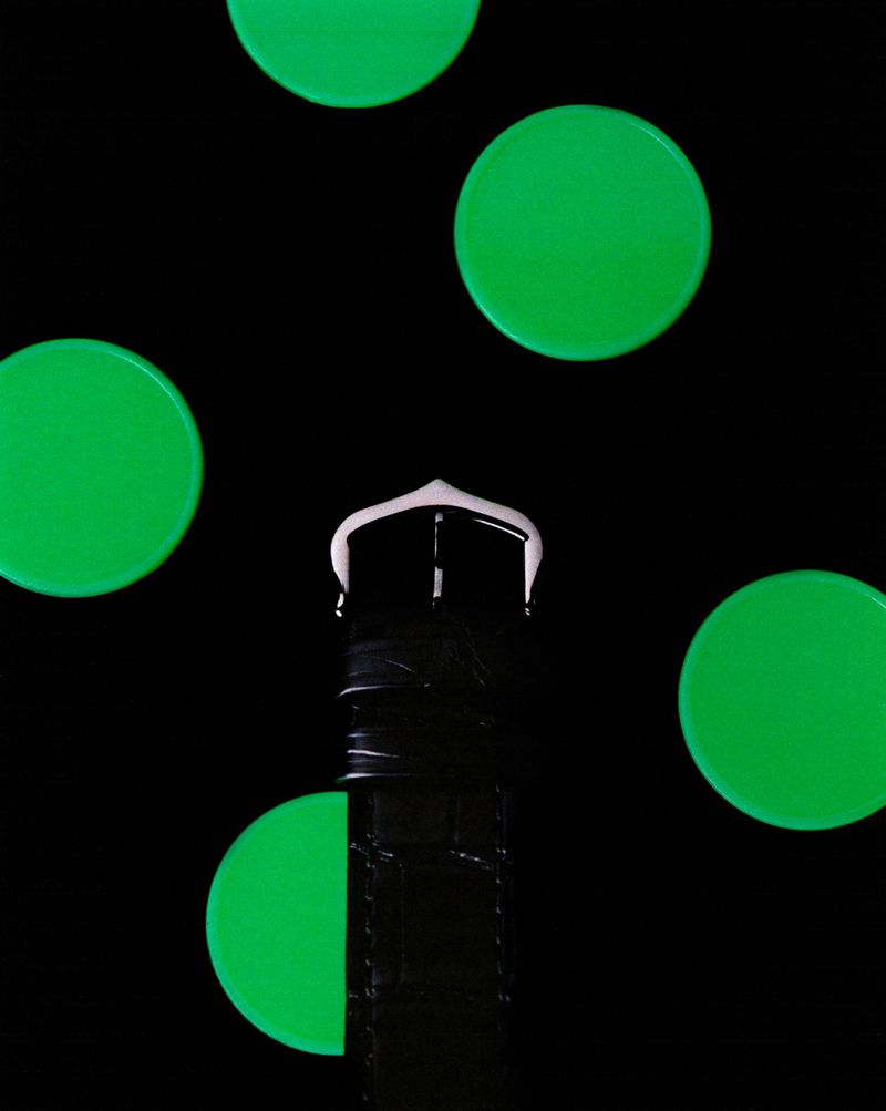 Cropped studio shot of a black wristwatch with a white buckle and several green glowing circles against a black background.