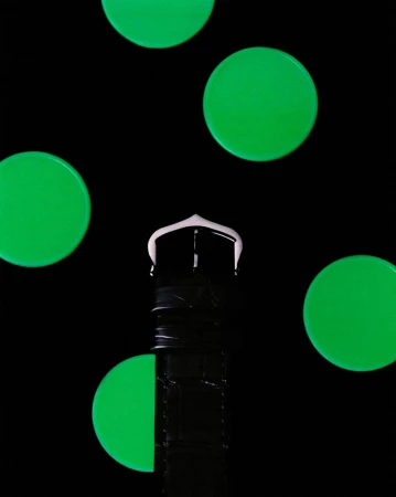 Cropped studio shot of a black wristwatch with a white buckle and several green glowing circles against a black background.